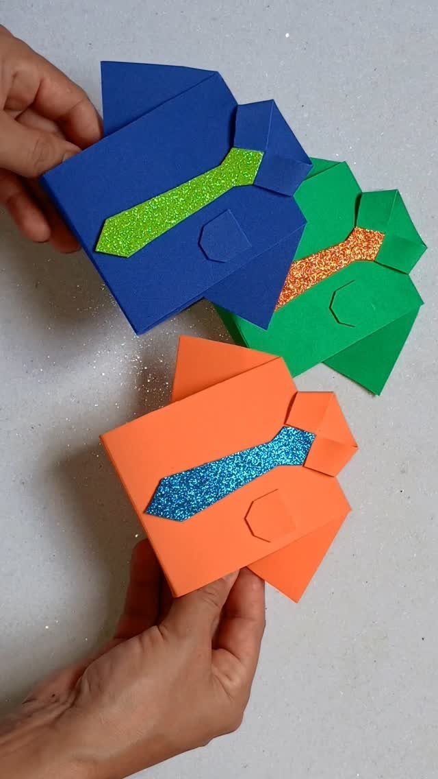 Three colorful paper shirt boxes with glittery ties held by two hands.