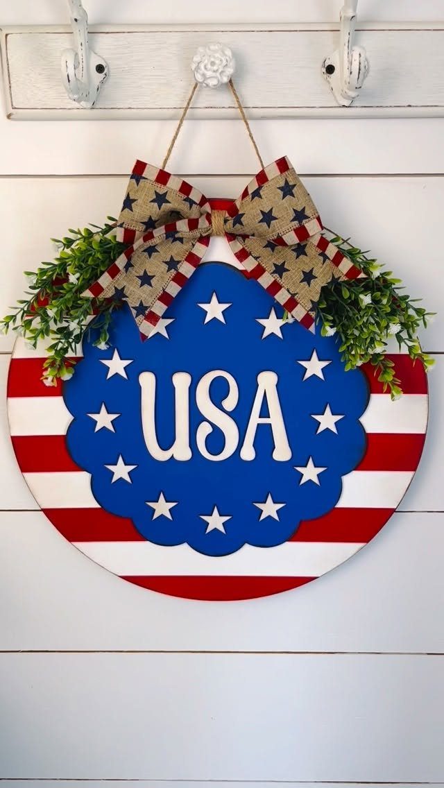 Round patriotic wooden door hanger with USA text, stars, and a star-patterned bow.