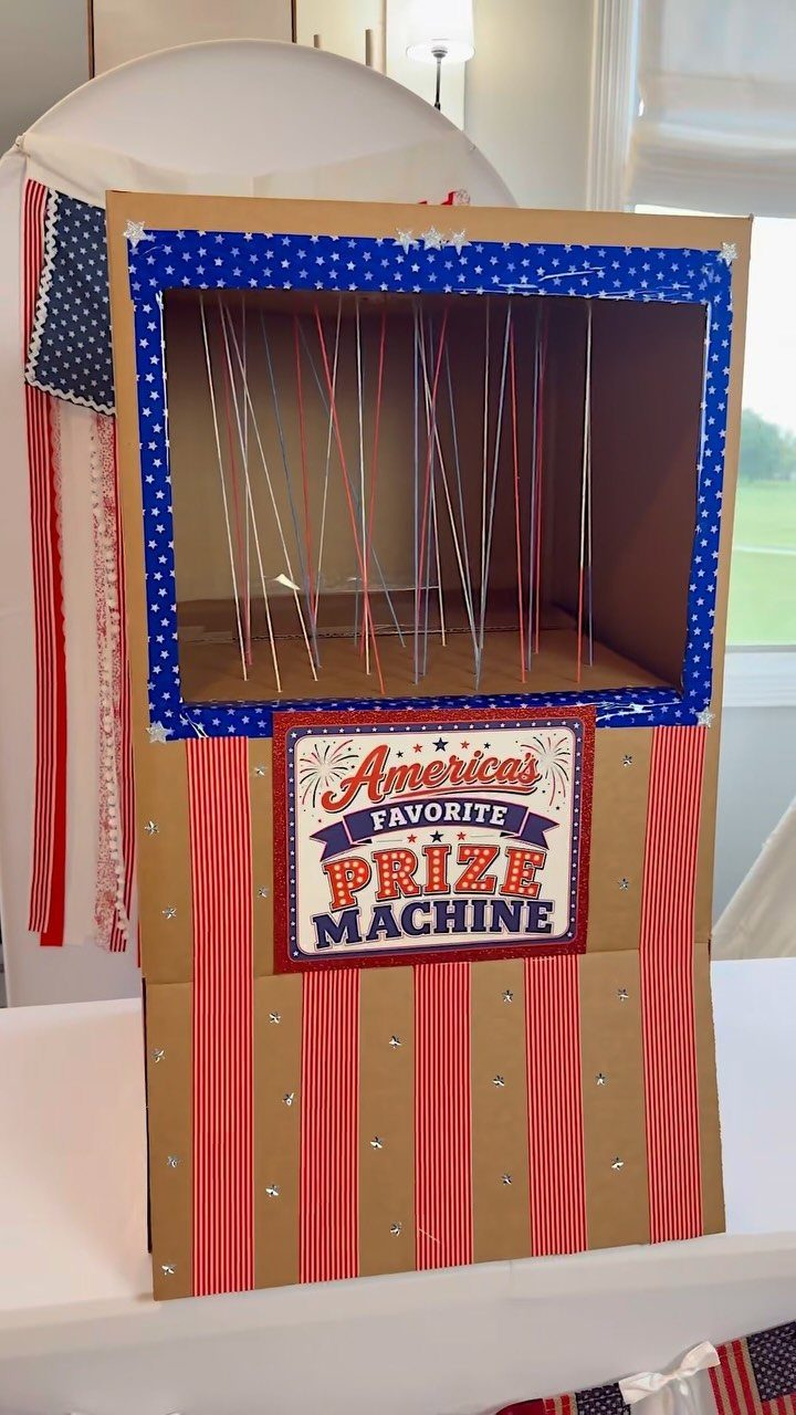 Cardboard prize machine decorated with red, white, and blue patriotic patterns and strings.