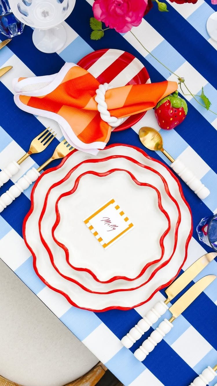 Red and white scalloped plates on a blue and white checkered tablecloth.
