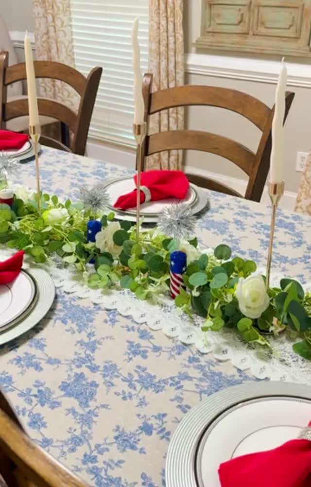 Festive dining table with blue floral cloth, green garland, and red napkins.