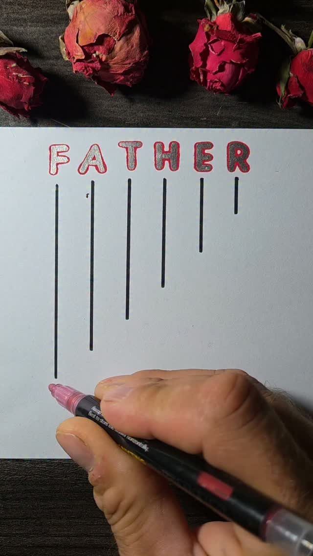 Hand coloring the word FATHER on a white sheet with dried red roses nearby.