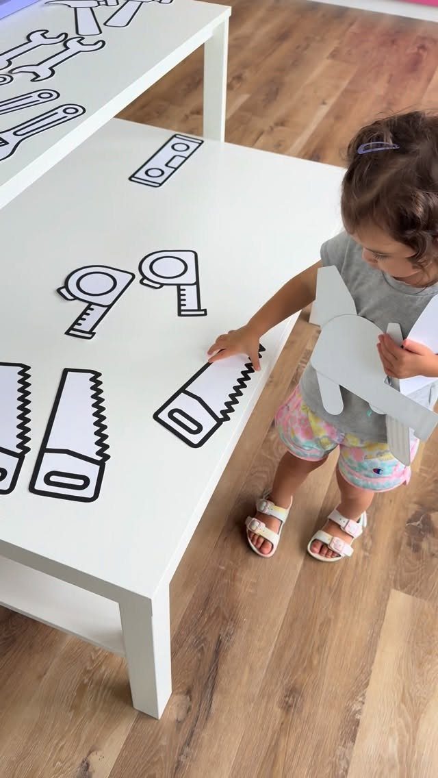 Young girl interacting with printed tool outlines on a white table.