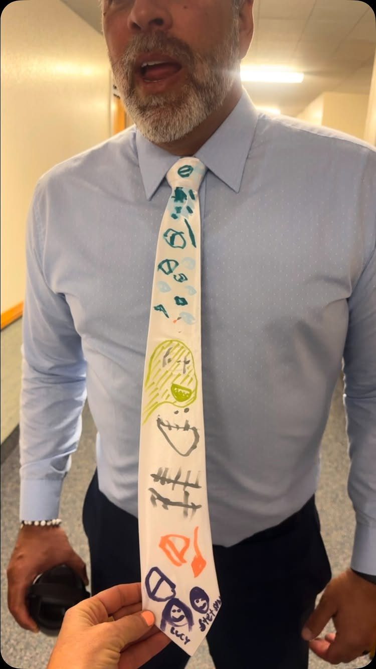 Man wearing a white necktie decorated with colorful children's drawings and scribbles.