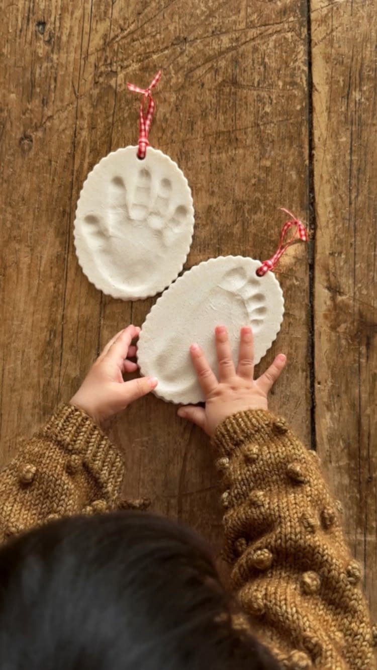 Child holding white salt dough ornaments with handprint and footprint impressions on wood