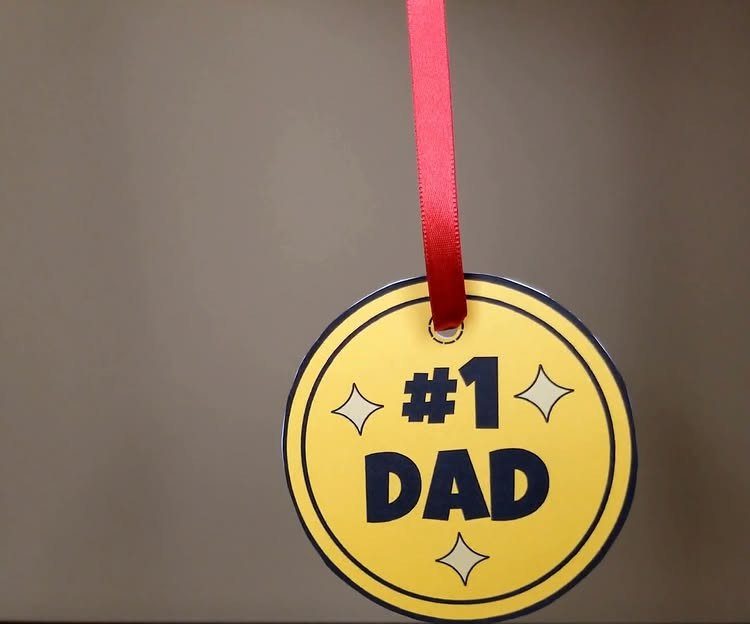 Yellow circular paper ornament with #1 DAD text hanging from red ribbon