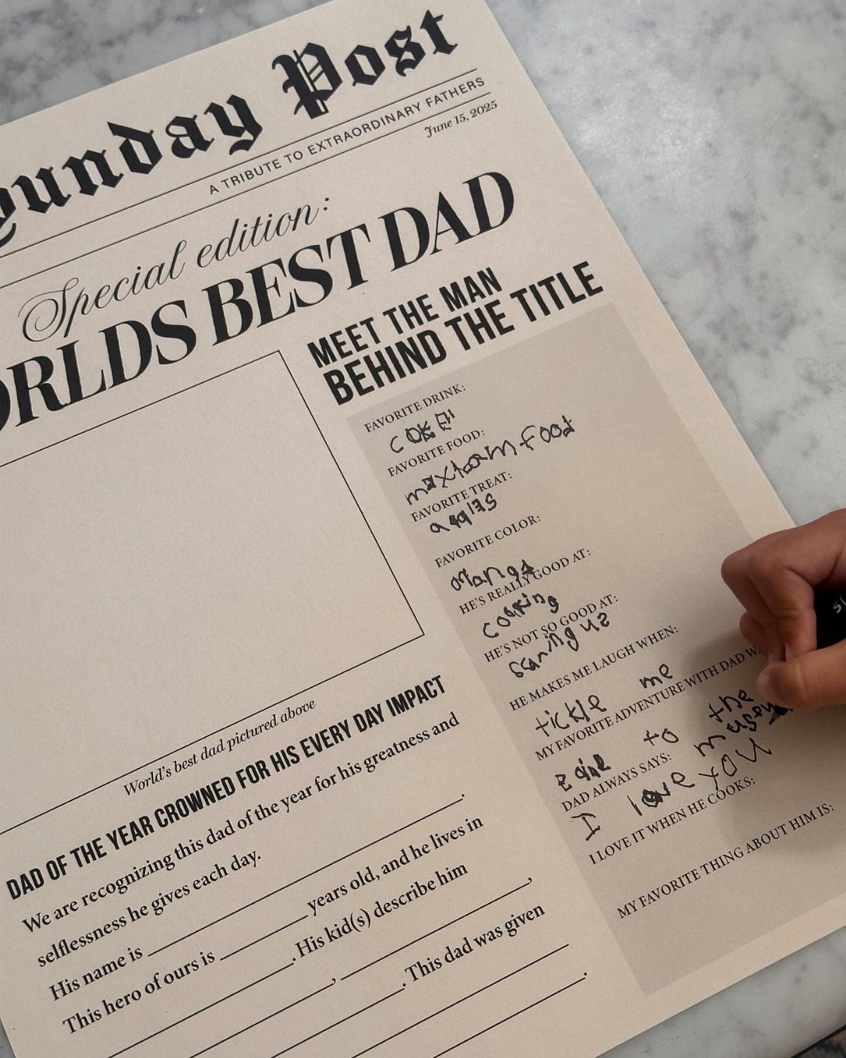 Hand filling out a printable Father's Day activity sheet on a marble table