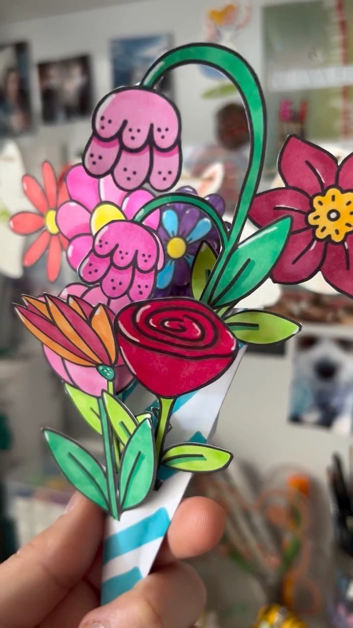 Hand holding a colorful paper cutout bouquet of flowers in a striped cone.