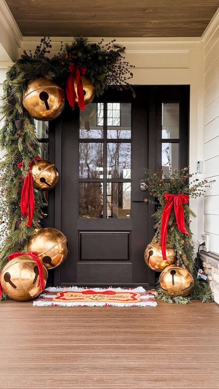 Black front door decorated with thick evergreen garland, large gold bells, and red ribbons.
