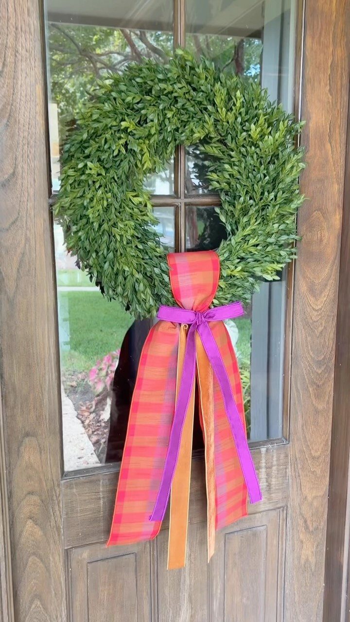 Green leafy wreath with a colorful striped ribbon on a wooden front door