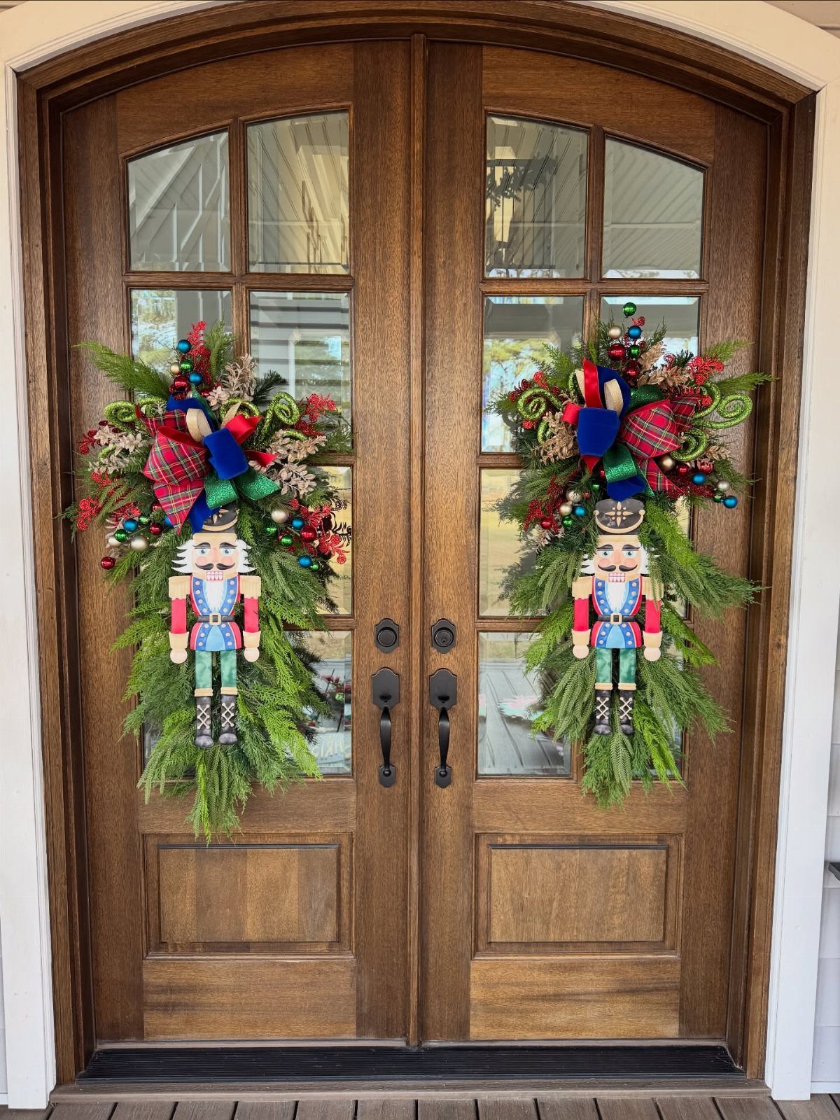 Nutcracker soldier figures centered in evergreen swags on double wooden front doors.