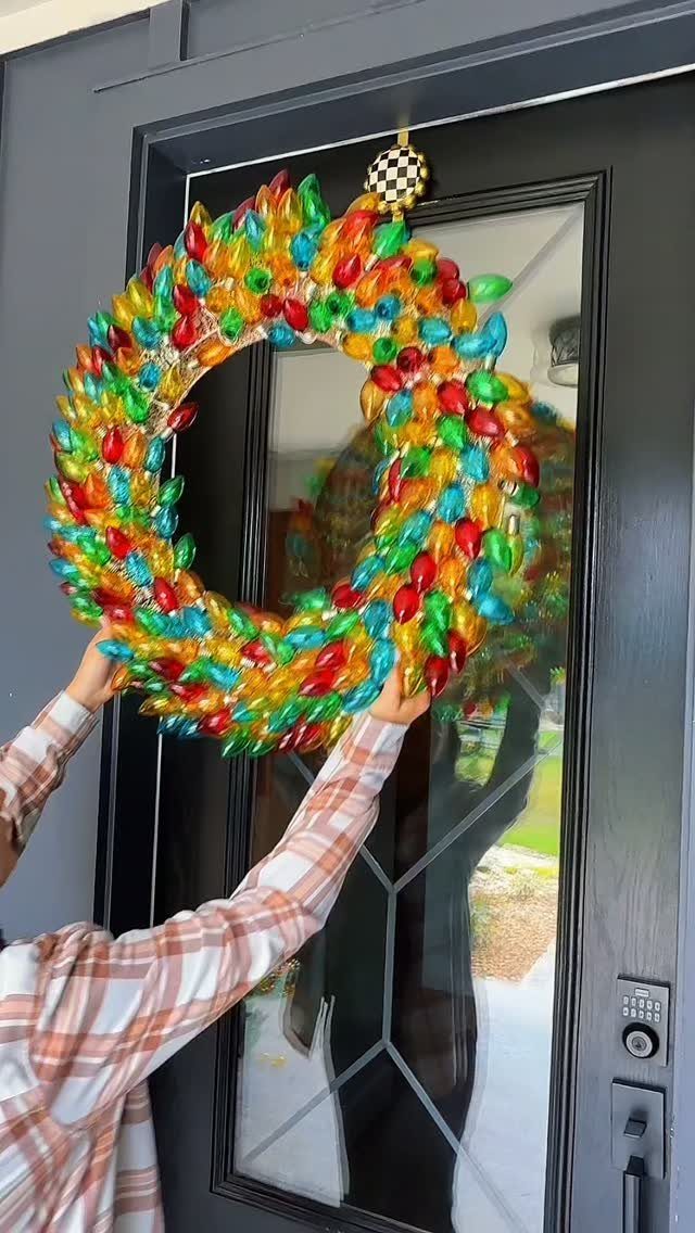 Colorful oversized light bulb wreath being placed on a black front door.