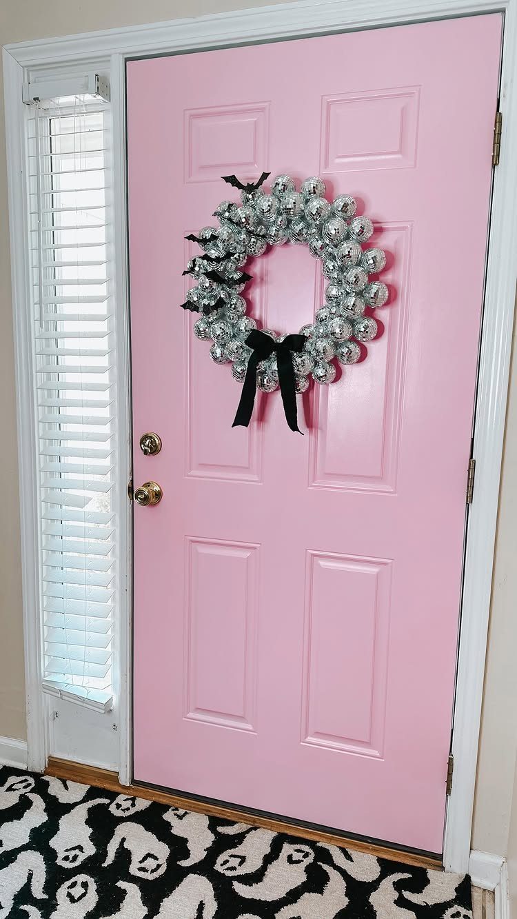 Pink front door decorated with a silver tinsel wreath and black bow.