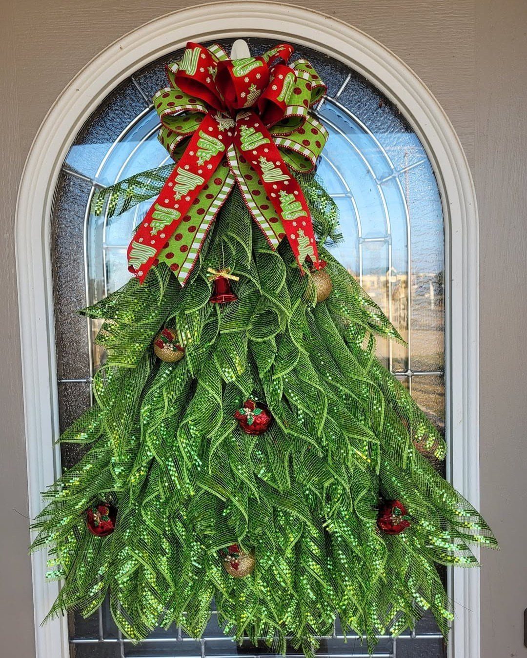 Tree-shaped green Christmas wreath with a large red bow on a white door