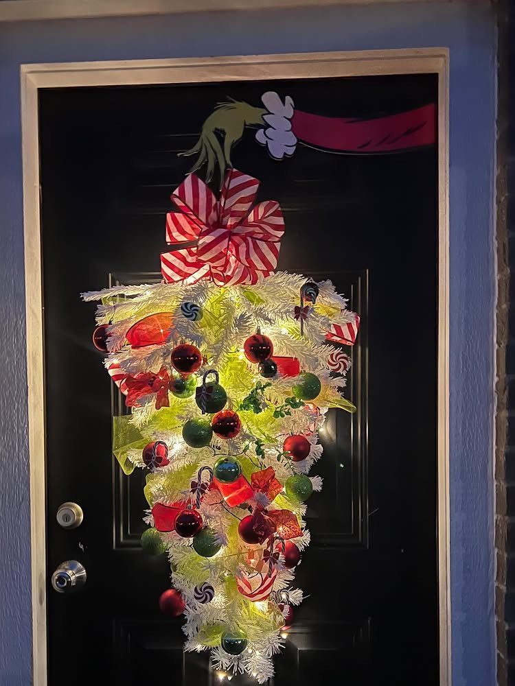Black front door decorated with a large, glowing Christmas ornament arrangement and red bow.