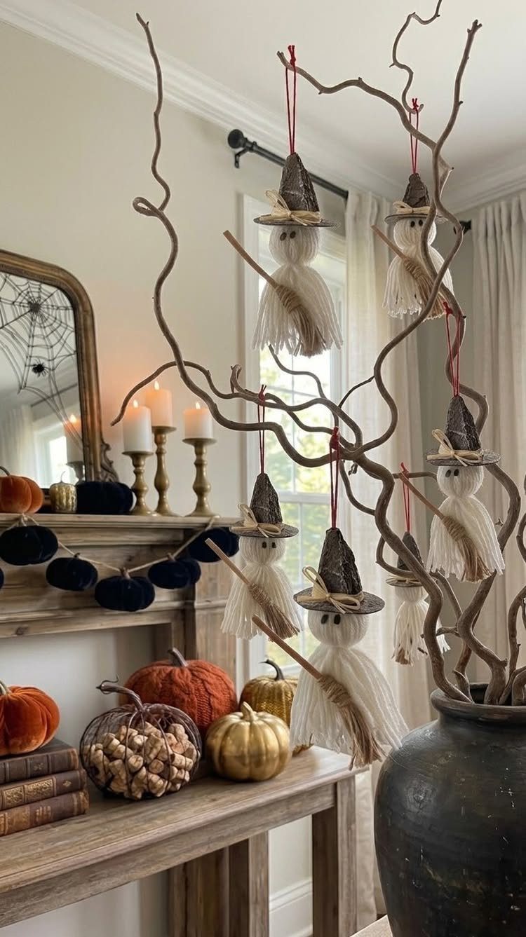 Handmade ghost ornaments with witch hats hanging from branches among autumn pumpkins.