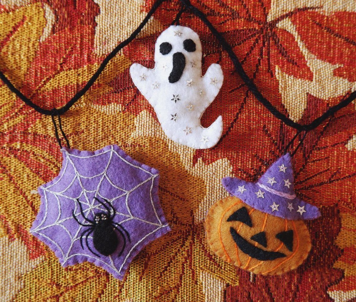 Felt ghost, spiderweb, and pumpkin wearing a witch hat on a black garland.