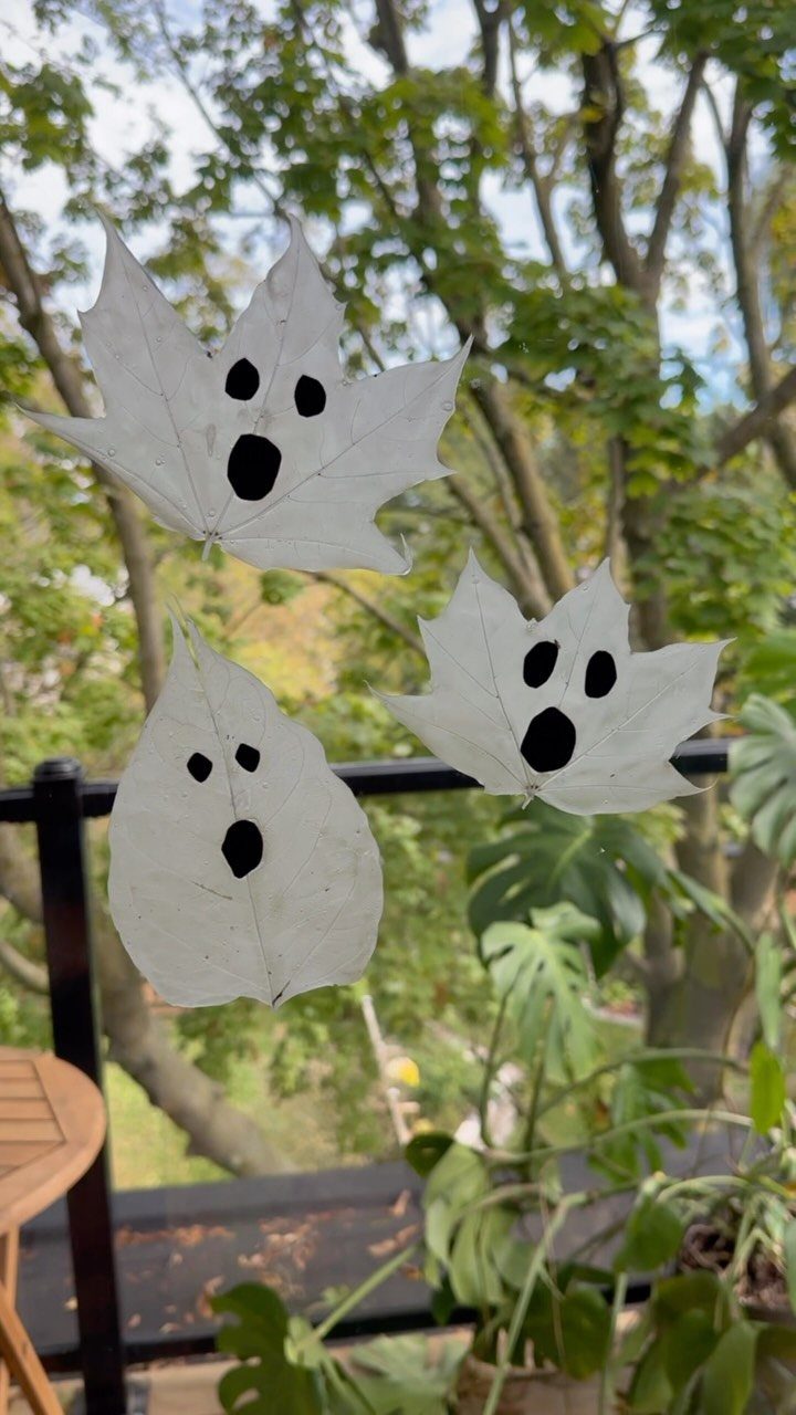White painted leaves with ghost faces hanging outdoors against green foliage