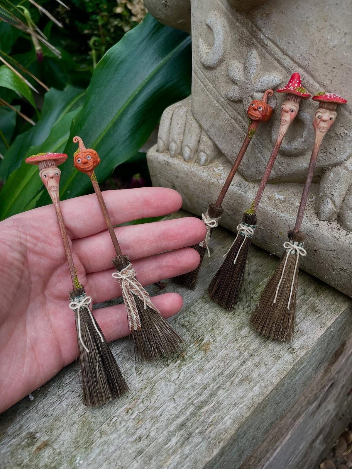 Tiny handmade witch's brooms with sculpted faces and hats on a wooden ledge.