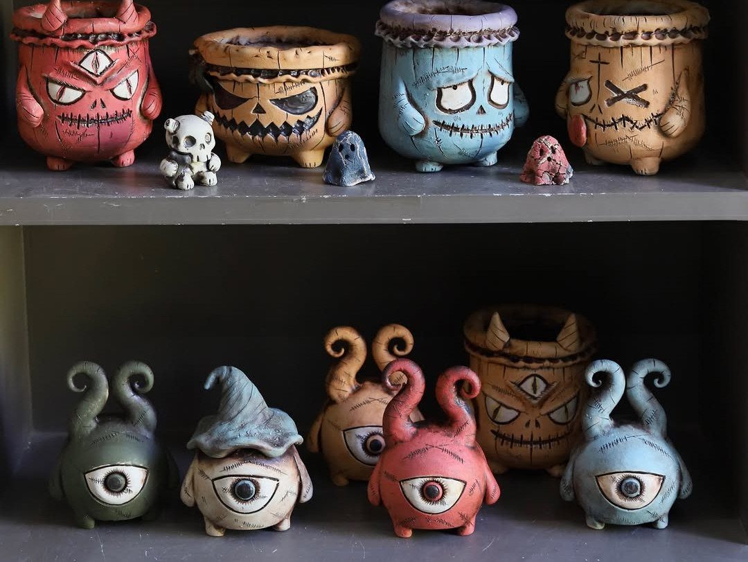 Handmade clay monster pinch pots with colorful paint and spooky faces on shelves.