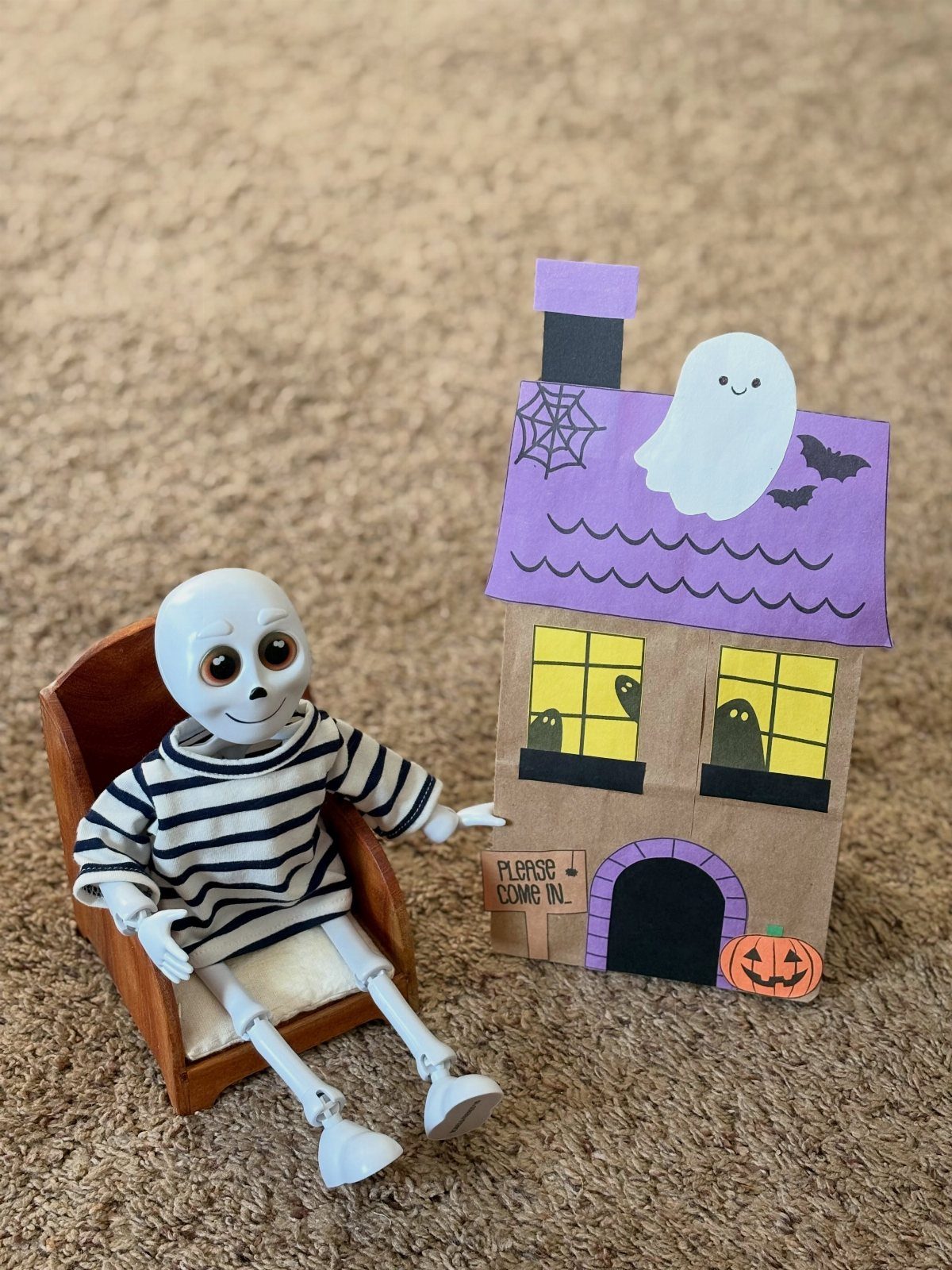 Paper bag haunted house with a purple roof next to a small skeleton figure.