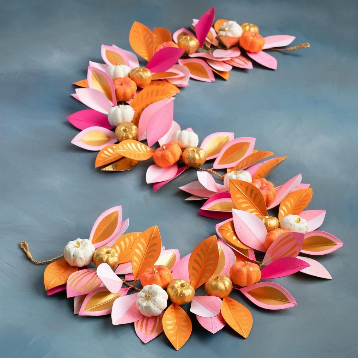 Paper leaf garland with small pumpkins in orange, pink, and gold colors.