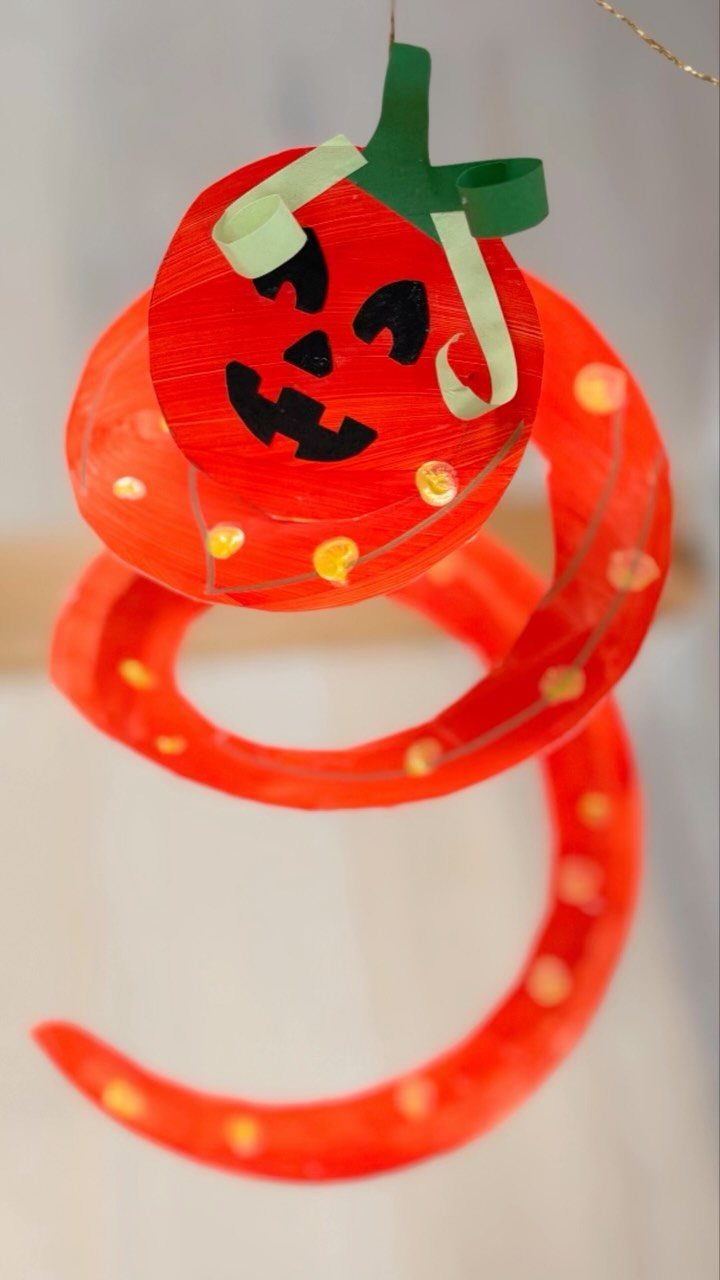 Paper plate pumpkin face attached to an orange spiraling paper strip decoration.