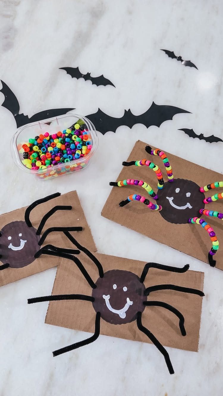 Handmade brown paper spiders with pipe cleaner legs and colorful beads on marble.