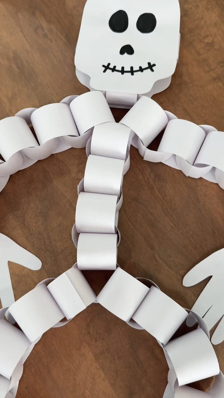 Paper skeleton craft made from white looped paper strips on a wooden background