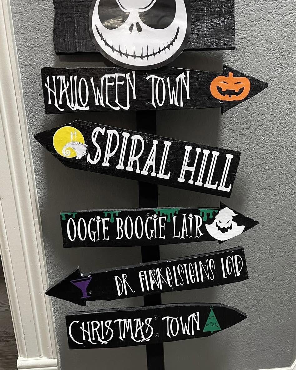 Black wooden directional signpost with spooky Halloween locations painted in white text.