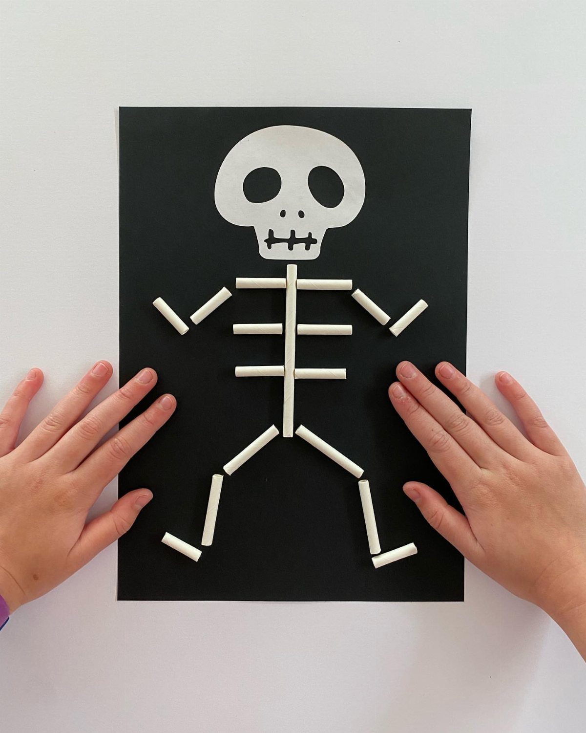 Skeleton craft made from white straws and a paper skull on black paper.