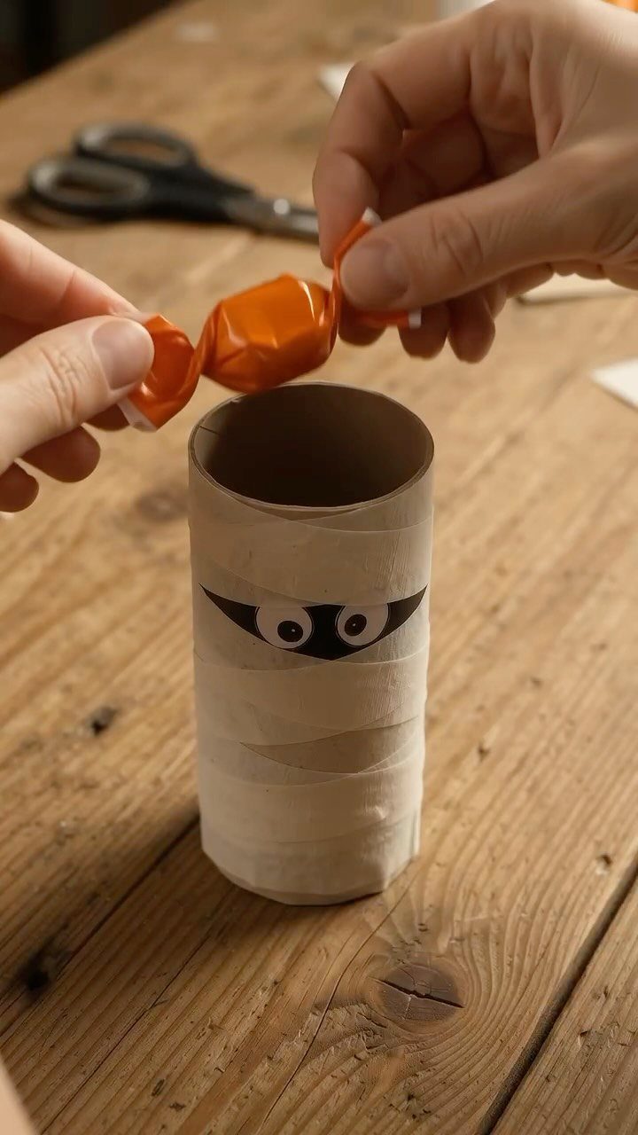 Mummy craft made from a toilet paper roll being filled with orange candy.