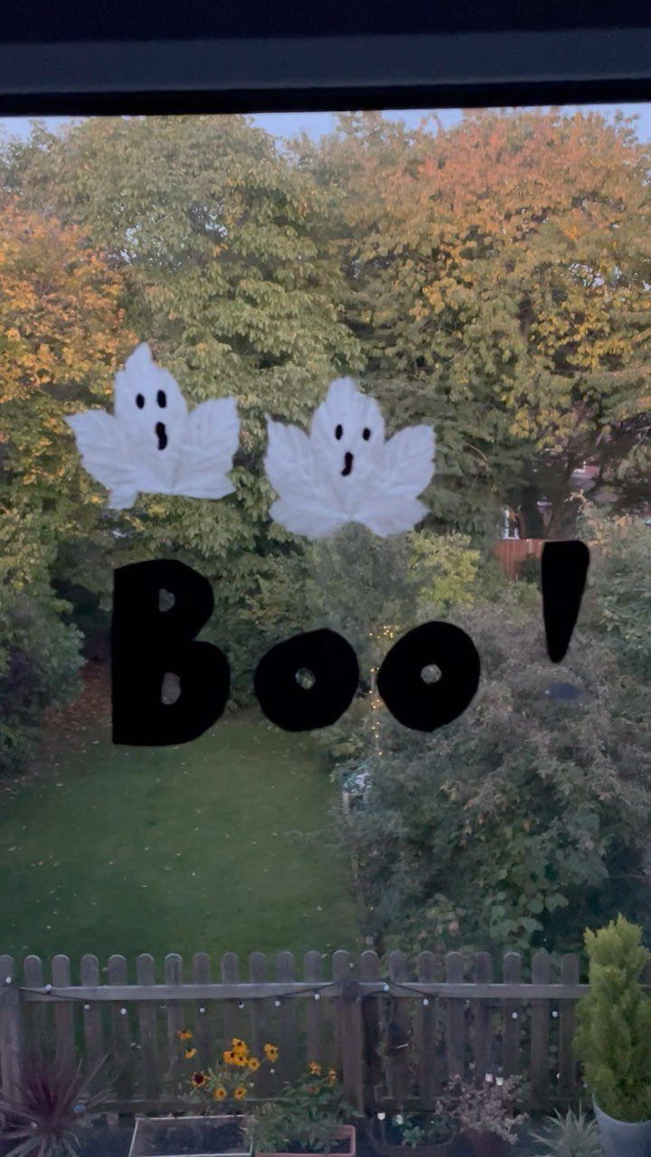 Paper ghost cutouts and Boo text on a window overlooking an autumn garden