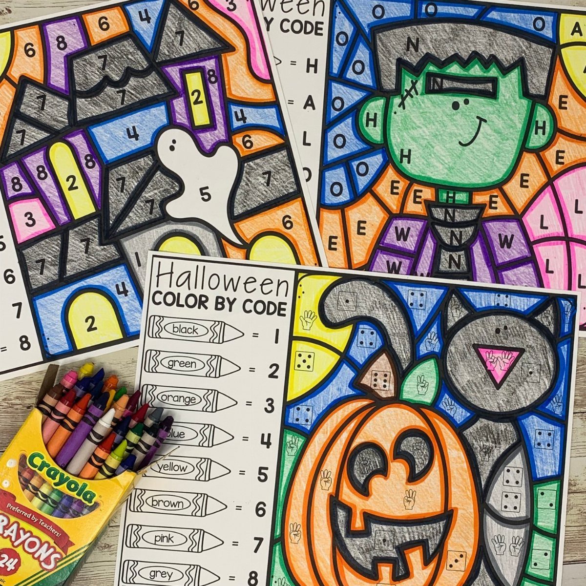 Completed Halloween color by code worksheets with a box of colorful crayons.