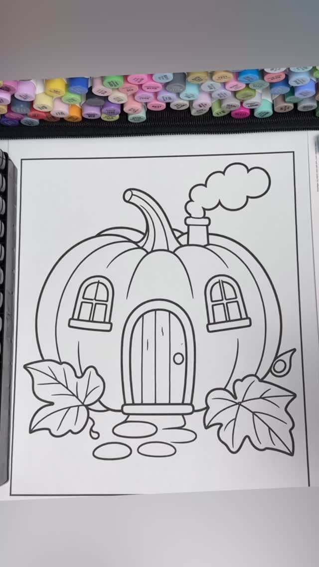 Pumpkin house coloring page printed on white paper with colorful markers above it.