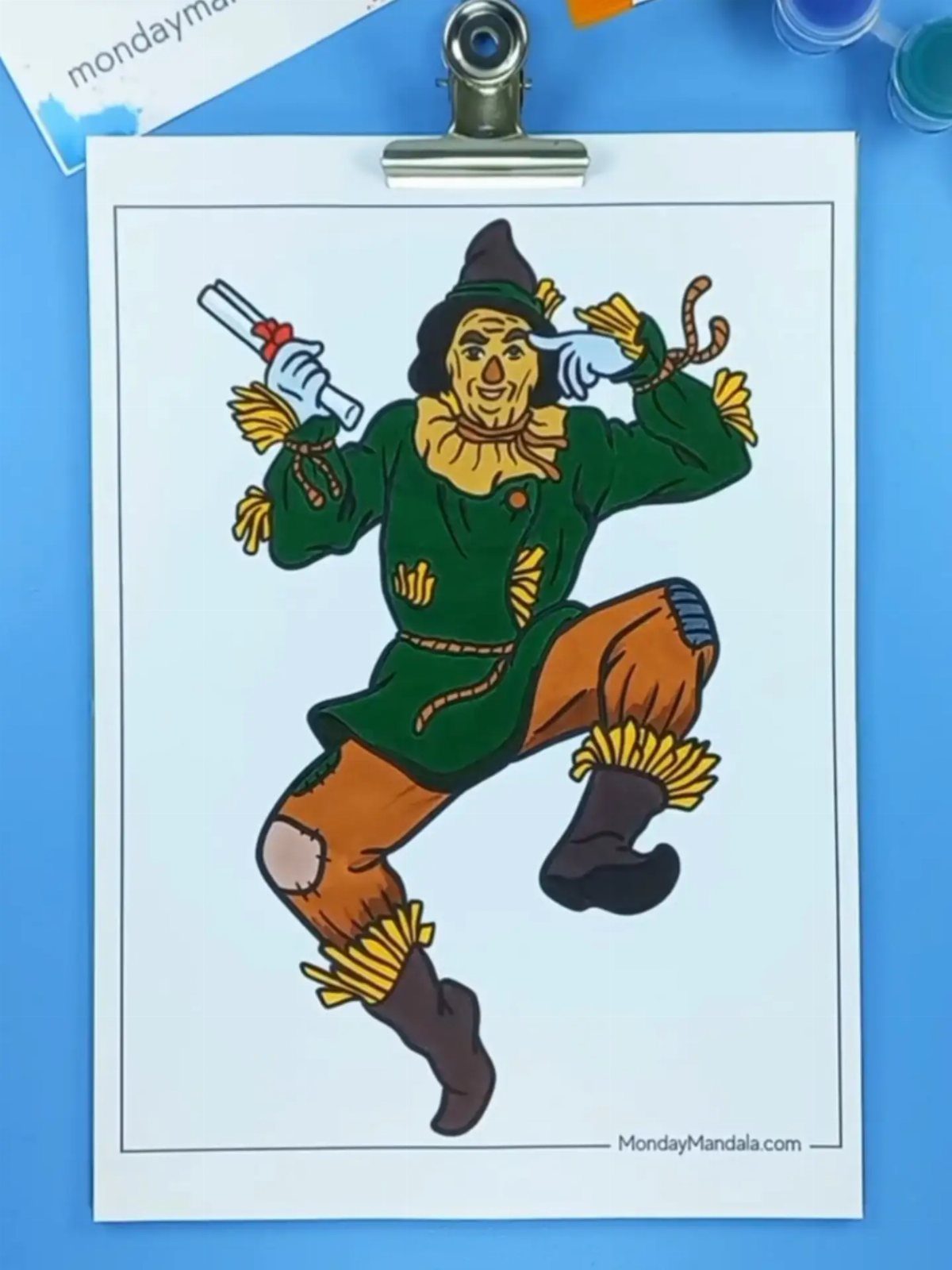 Colored scarecrow drawing on a white page clipped to a blue surface.