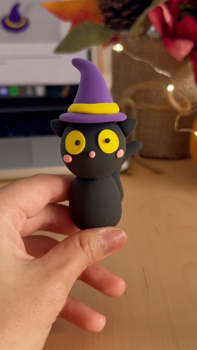 Small black clay cat wearing a purple witch hat held by a hand.