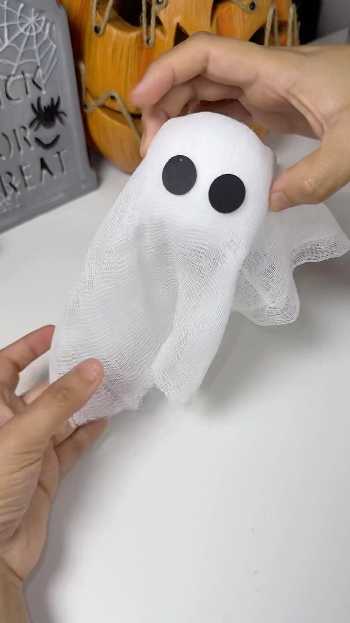 Small white gauze ghost with black eyes held by two hands.