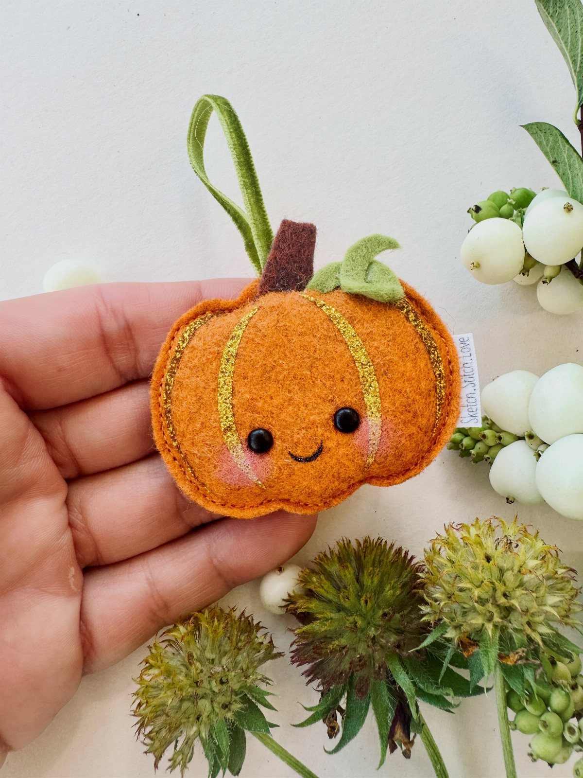 Small orange felt pumpkin ornament with a cute face held in a hand.