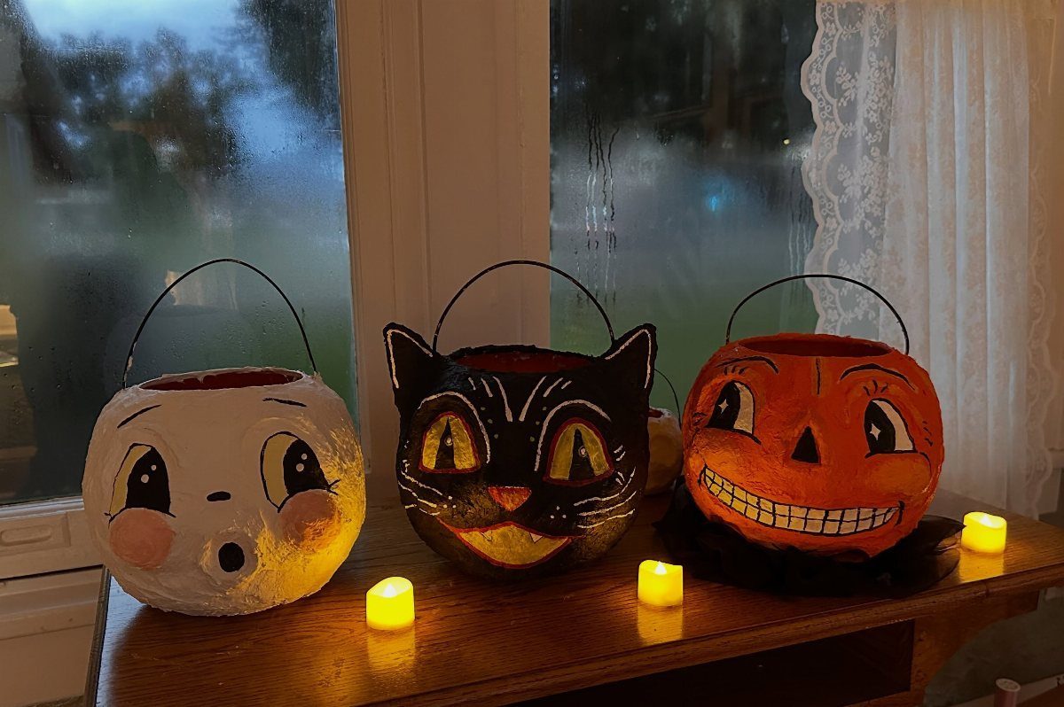 Handmade ghost, cat, and pumpkin buckets on a wooden ledge with tea lights.