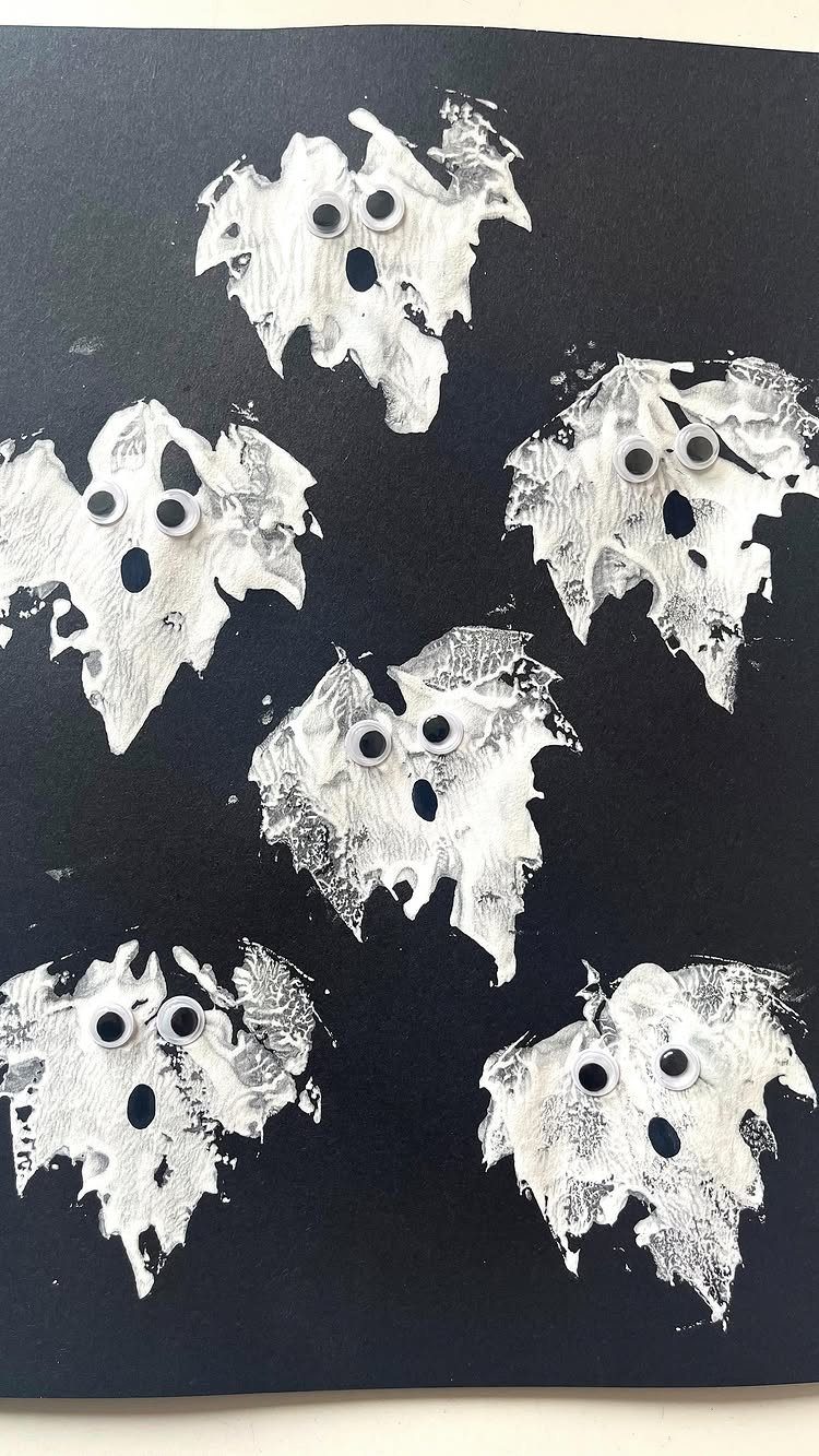 White painted leaves as ghosts with googly eyes on black paper background.