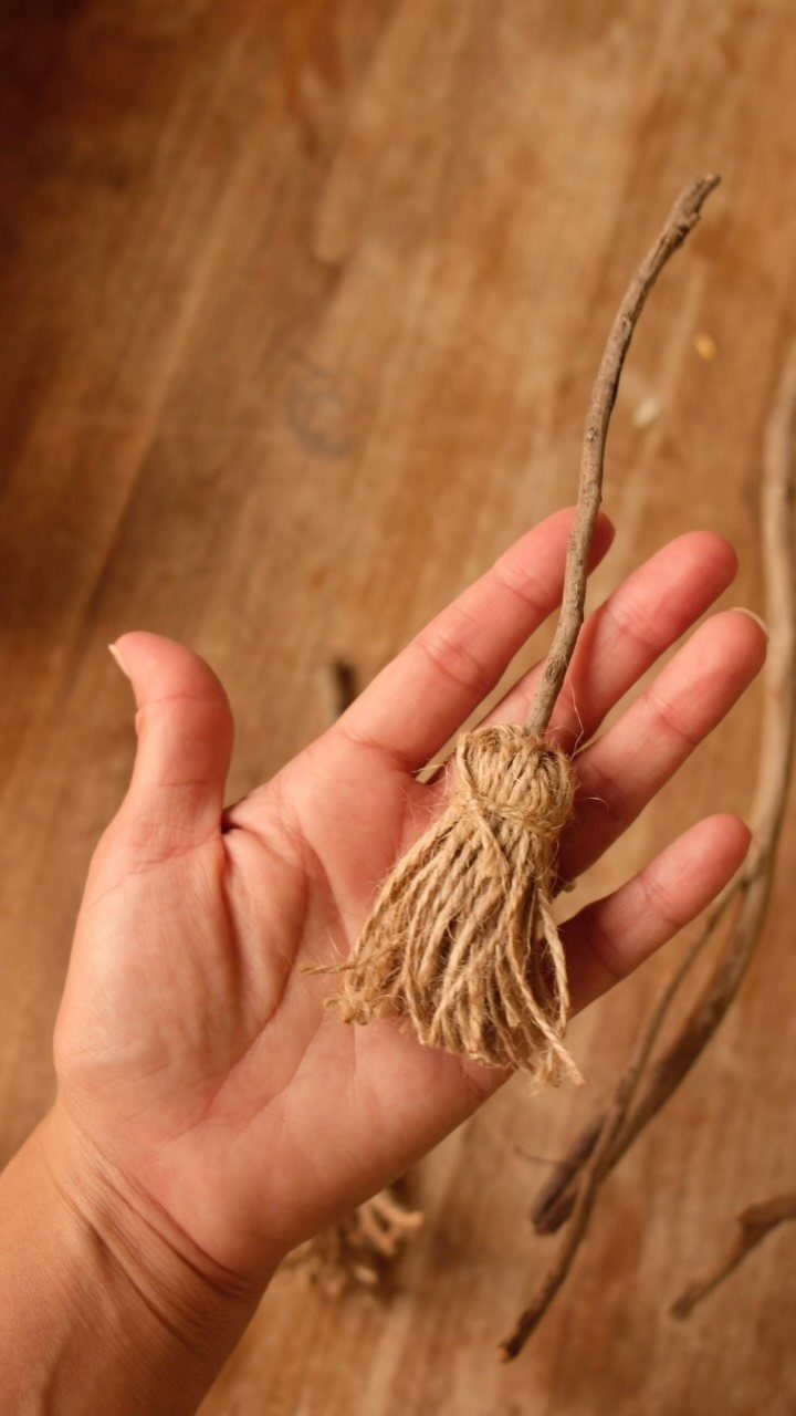 Hand holding a mini witch's broom made from a twig and twine.