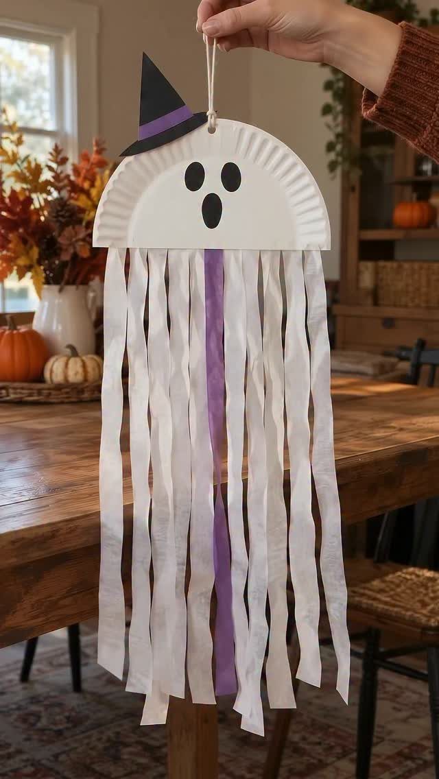 Paper plate ghost wearing a witch hat with long hanging paper strips.
