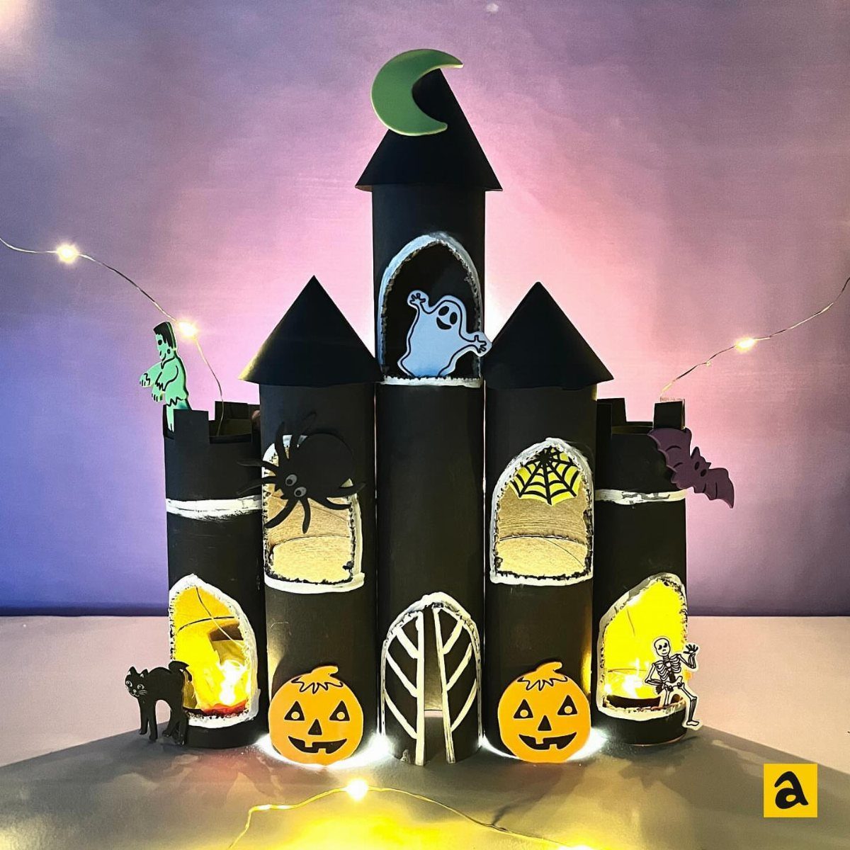 Haunted house craft made from black paper rolls with glowing windows and spooky decorations.