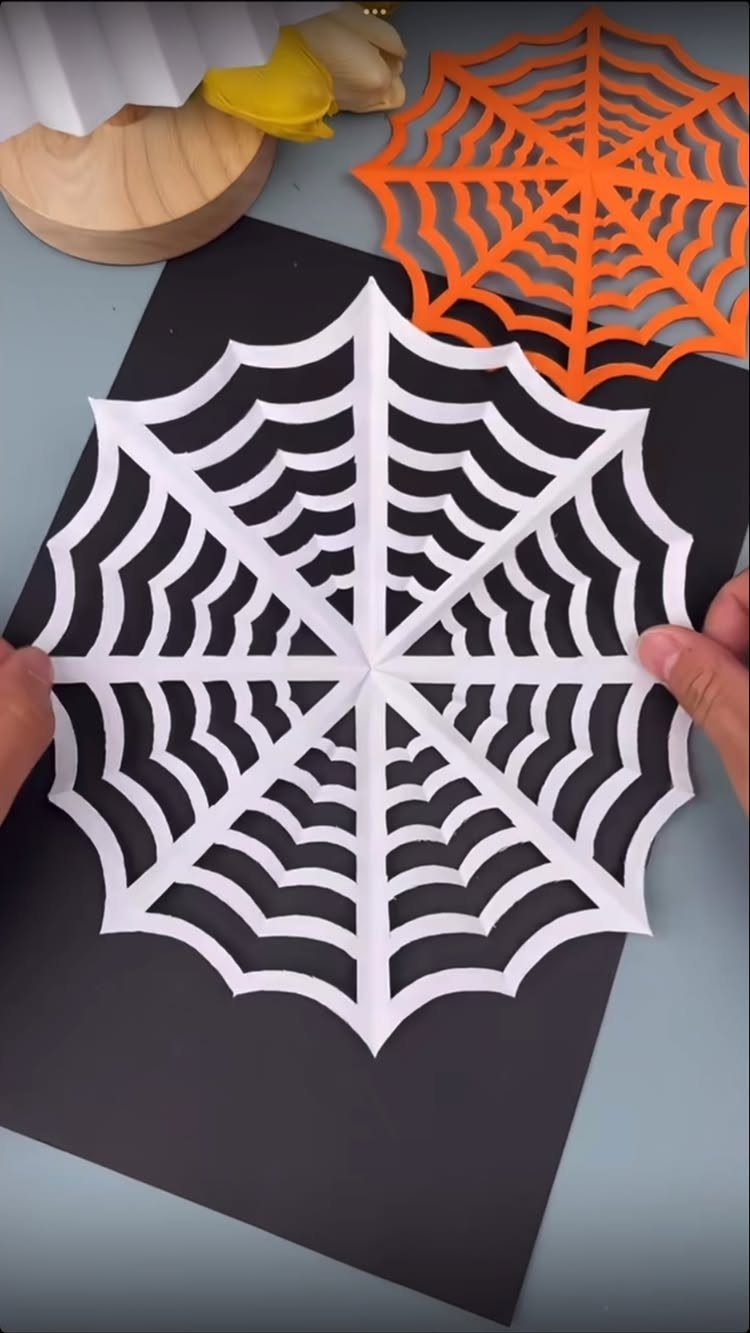 White and orange paper spiderweb cutouts on a black background for Halloween crafts.
