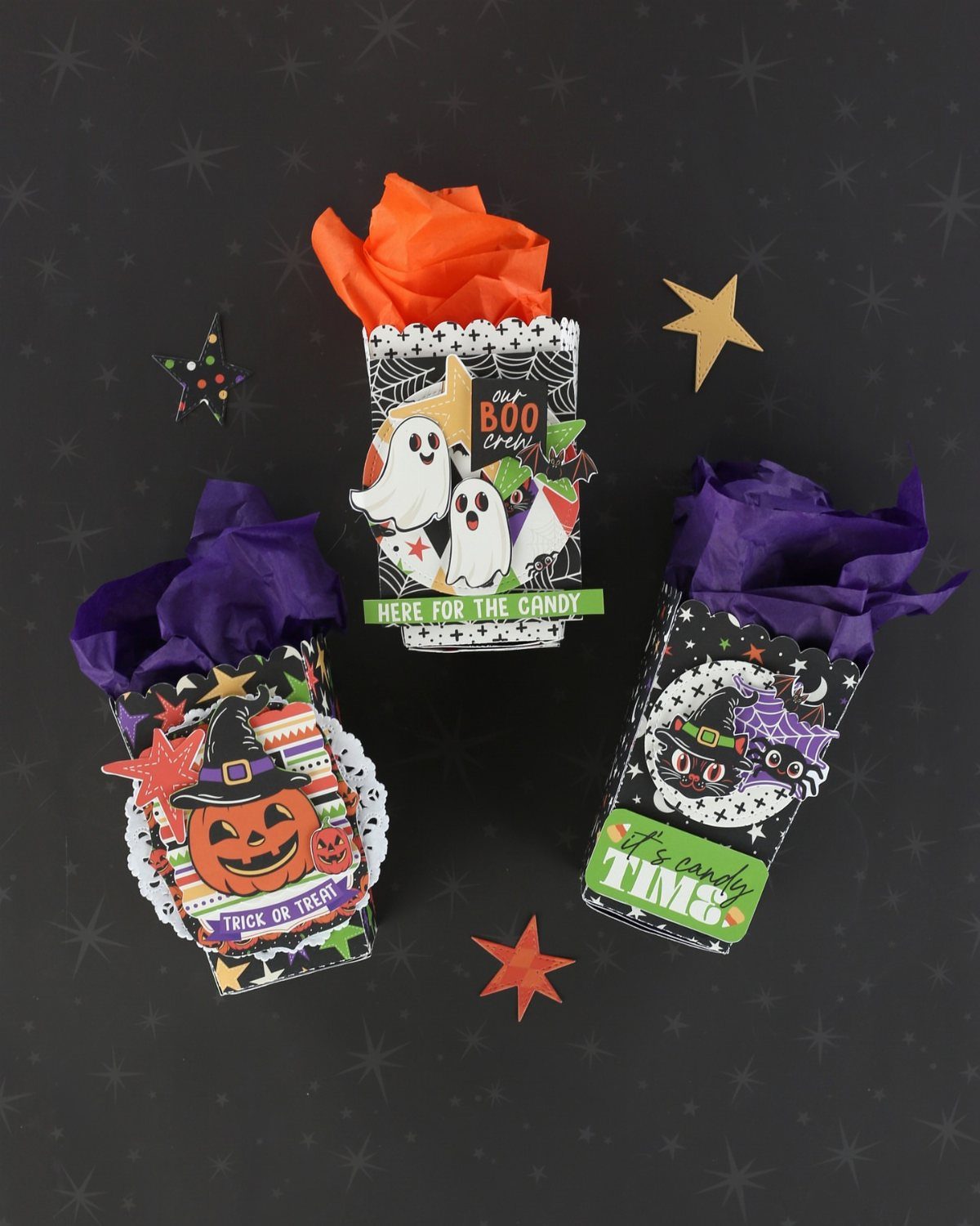 Three printed Halloween treat boxes with ghosts and pumpkins filled with colorful tissue paper.