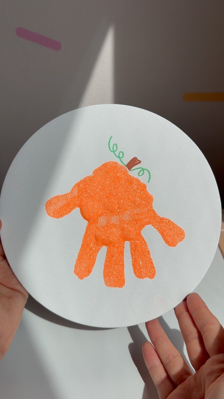 Orange handprint painted as a pumpkin on a white circular paper background.