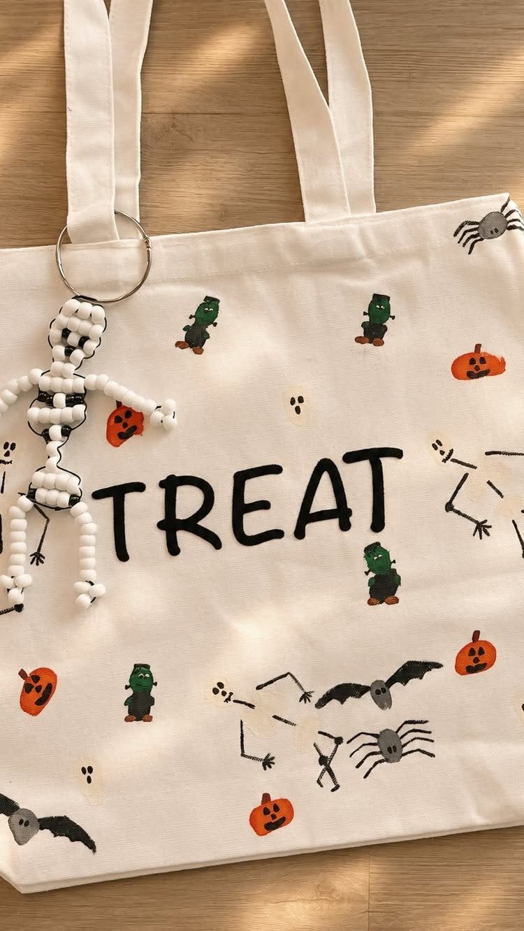 White canvas treat bag decorated with Halloween drawings and a beaded skeleton keychain.