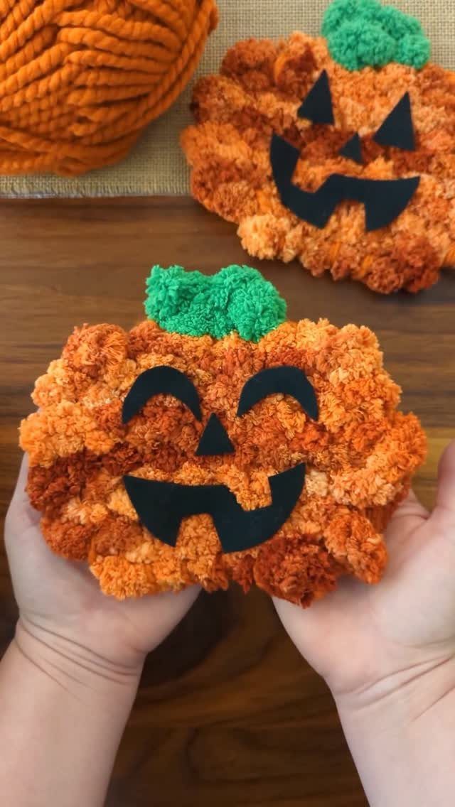 Two orange yarn pumpkins with black paper faces and green yarn stems.