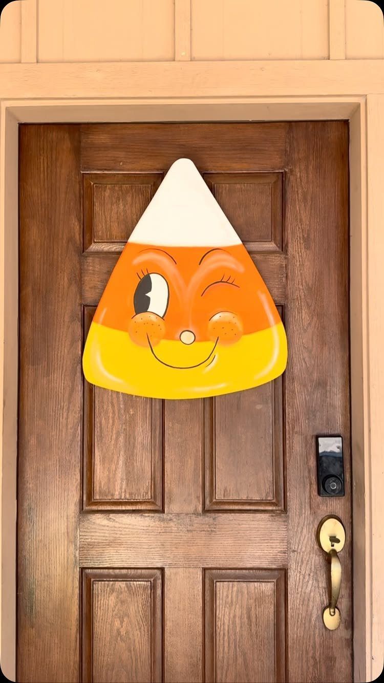 Winking cartoon candy corn decoration attached to a brown wooden front door.